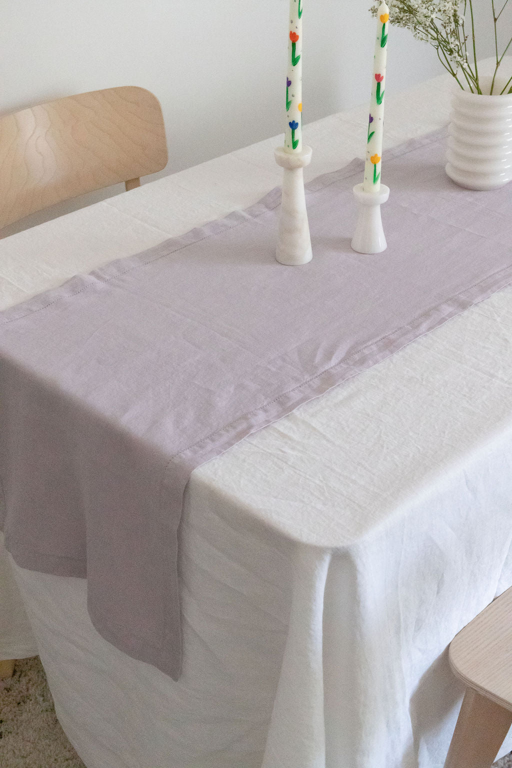 Dining table styled with an off-white linen tablecloth and a lavender linen table runner, creating a soft and elegant table setting.